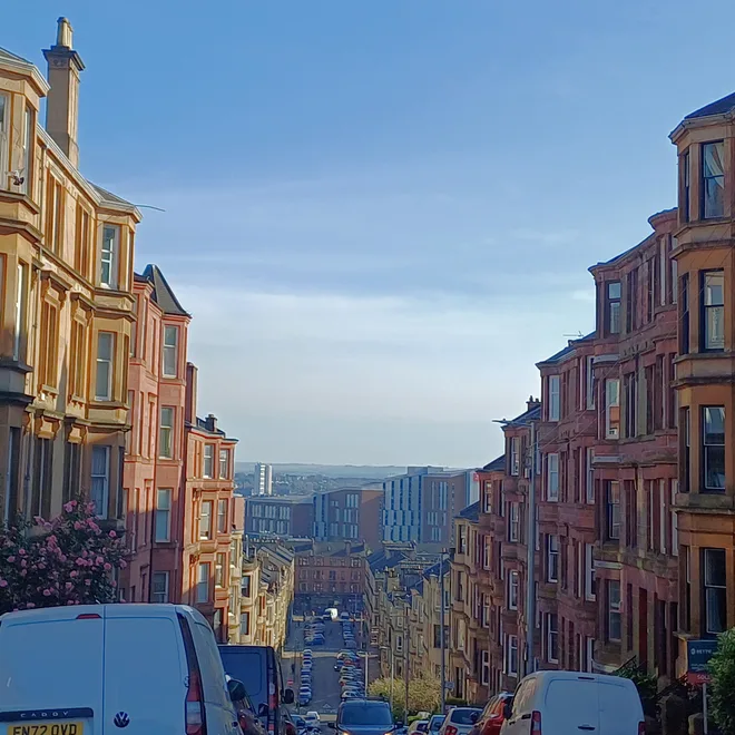 Glasgow street of sandstone tenements descending toward the city skyline