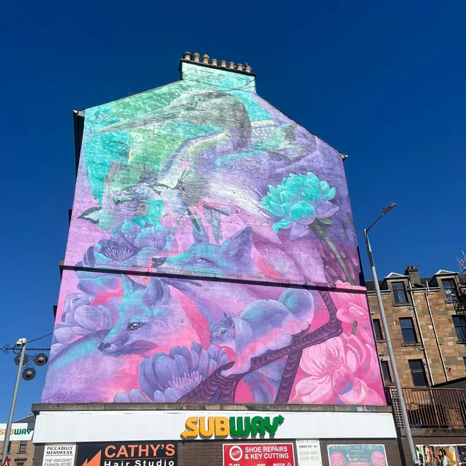 Pink and teal heron and fox mural above a row of shops on a Glasgow tenement